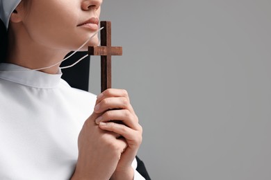Photo of Nun with cross praying to God on grey background, closeup. Space for text