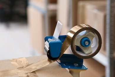 Photo of Taping cardboard box with adhesive tape dispenser indoors, closeup. Space for text