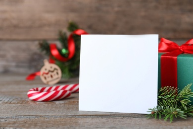 Blank Christmas card, gift box and fir branches on wooden table, space for text