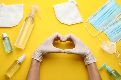 Person in gloves showing heart gesture surrounded by medical items on yellow background, top view