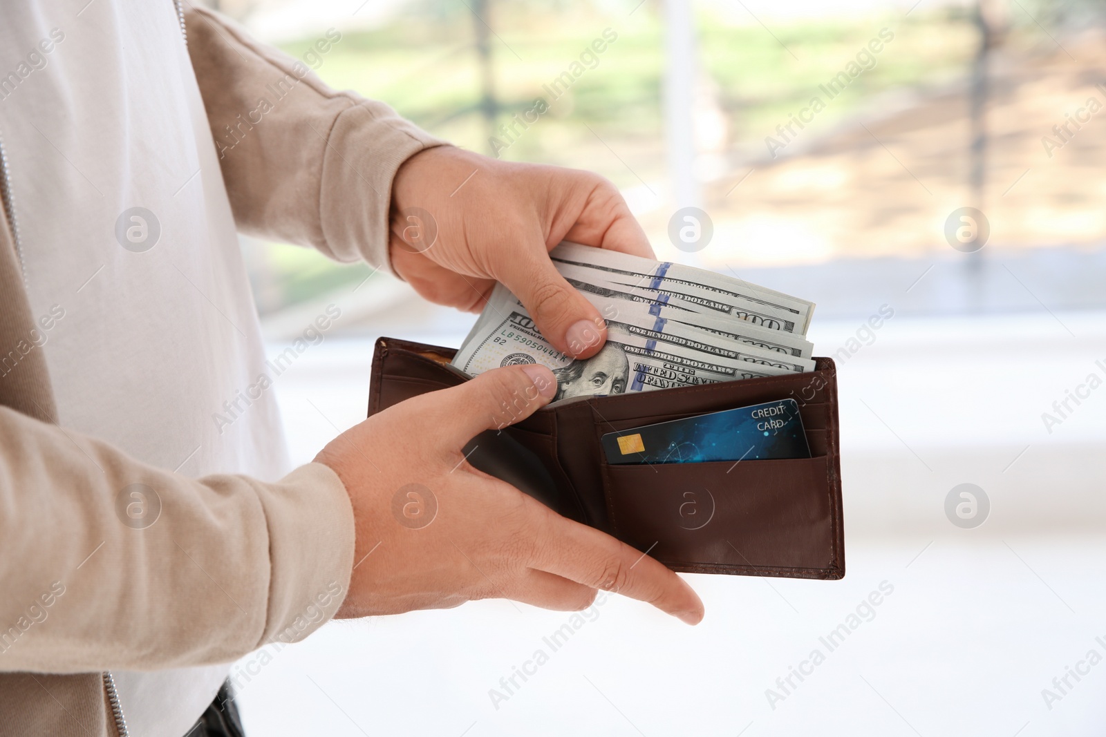 Photo of Man holding wallet with money on blurred background, closeup