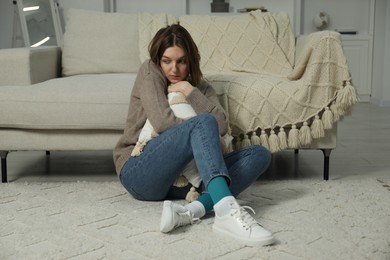 Photo of Sad young woman sitting on floor at home