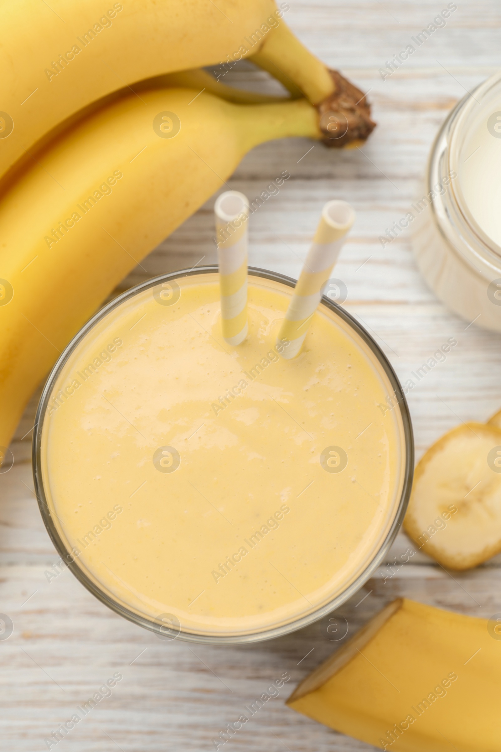 Photo of Glass of tasty banana smoothie with straws and ingredients on white wooden table, flat lay