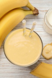 Photo of Glass of tasty banana smoothie with straws and ingredients on white wooden table, flat lay