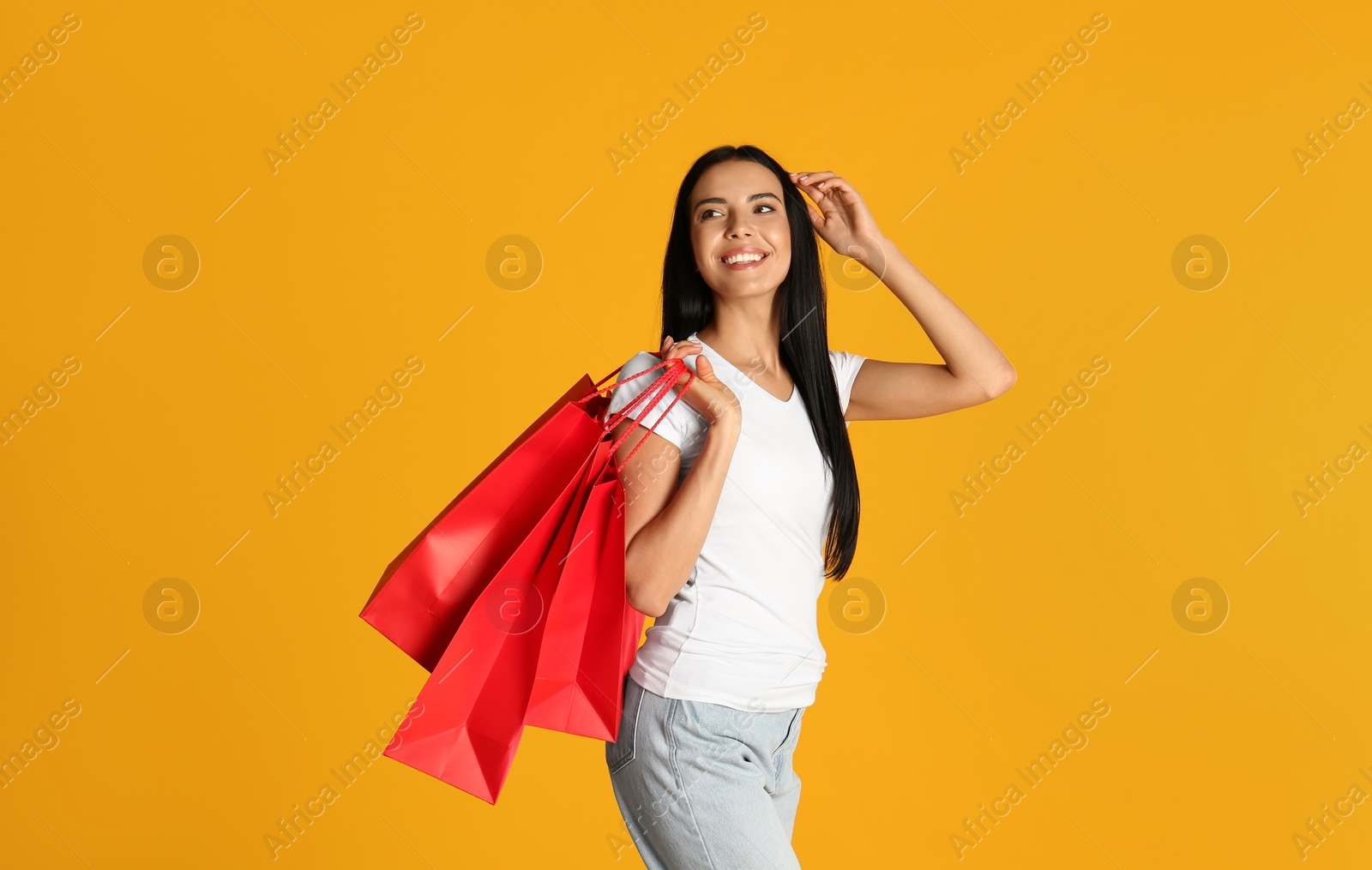 Photo of Beautiful young woman with paper shopping bags on yellow background