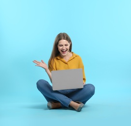 Emotional young woman with laptop celebrating victory on color background