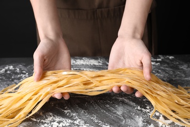 Woman holding raw egg noodles over grey table, closeup
