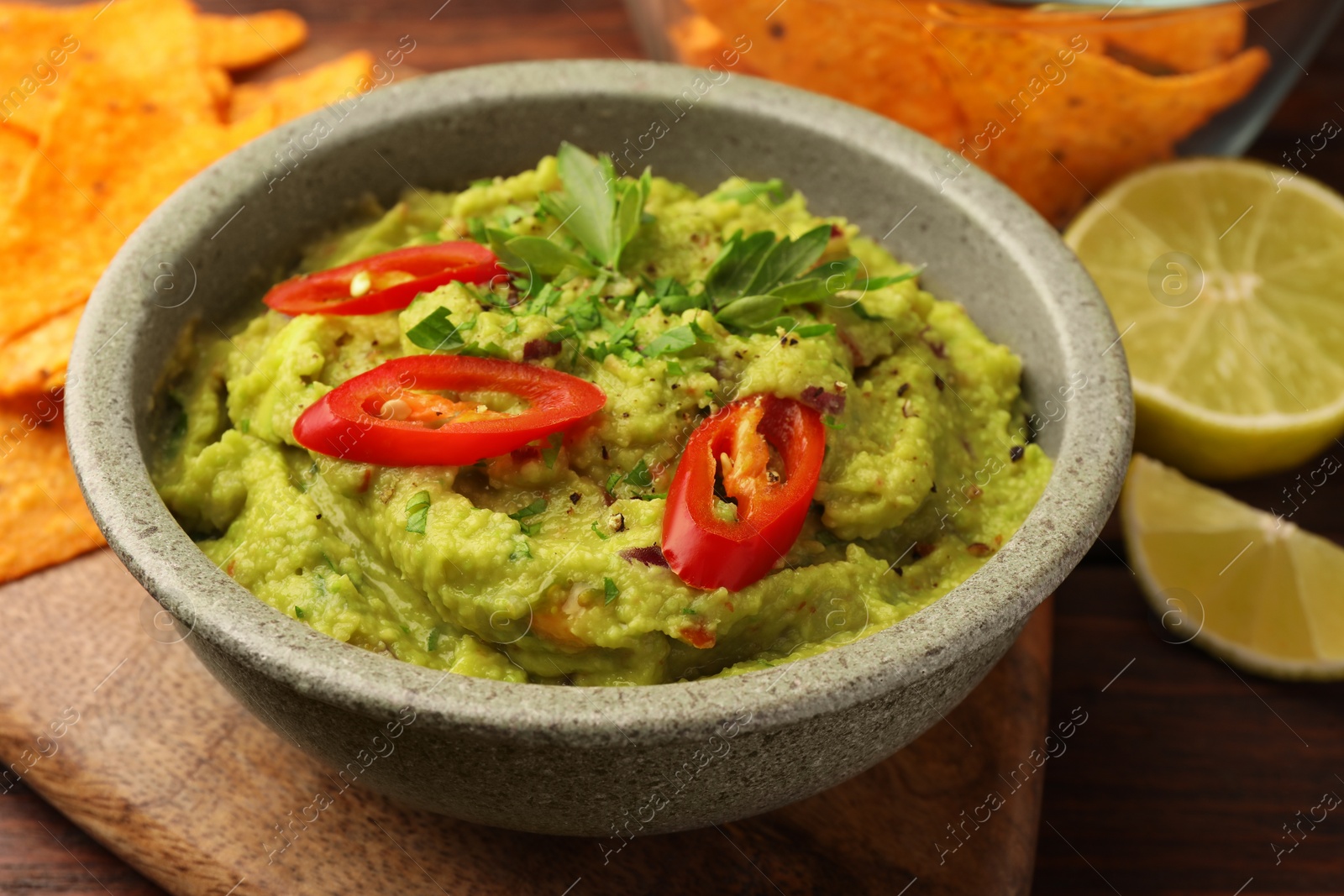 Photo of Bowl of delicious guacamole, lime and tortilla chips on wooden table, closeup