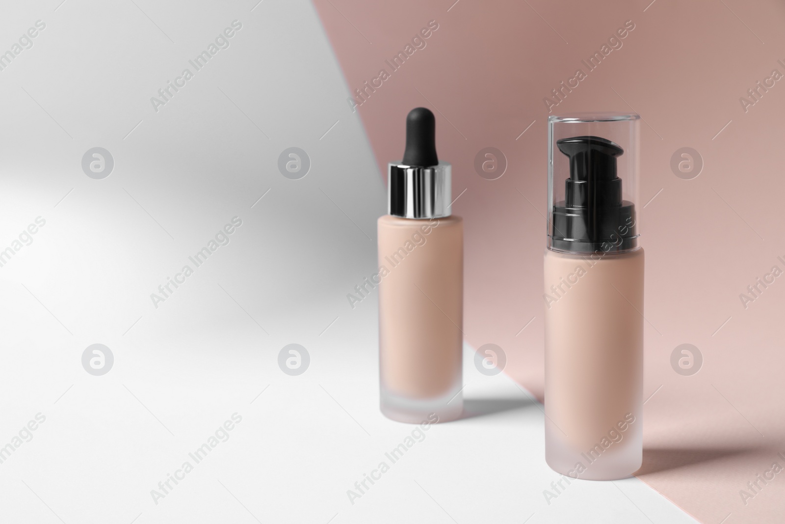 Photo of Bottles of skin foundation on color background, space for text. Makeup product