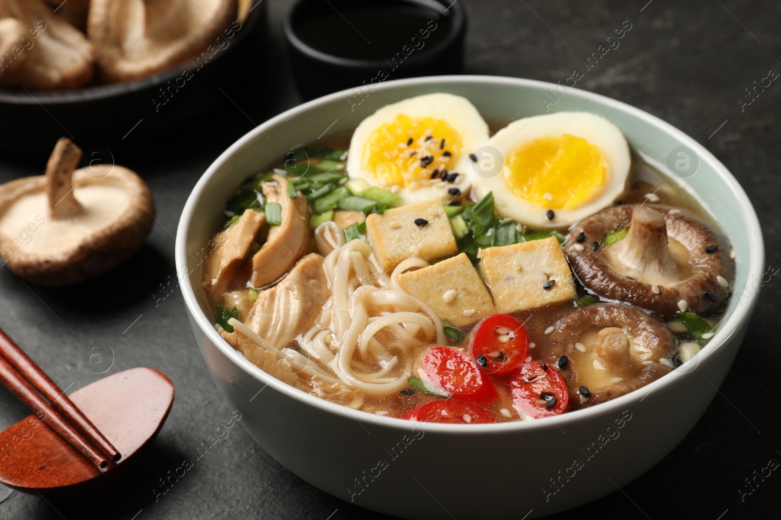 Photo of Noodle soup. Bowl of delicious ramen, ingredients and chopsticks on black table, closeup