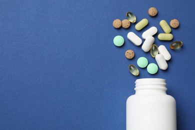 Photo of Different vitamin pills and bottle on blue background, top view. Space for text