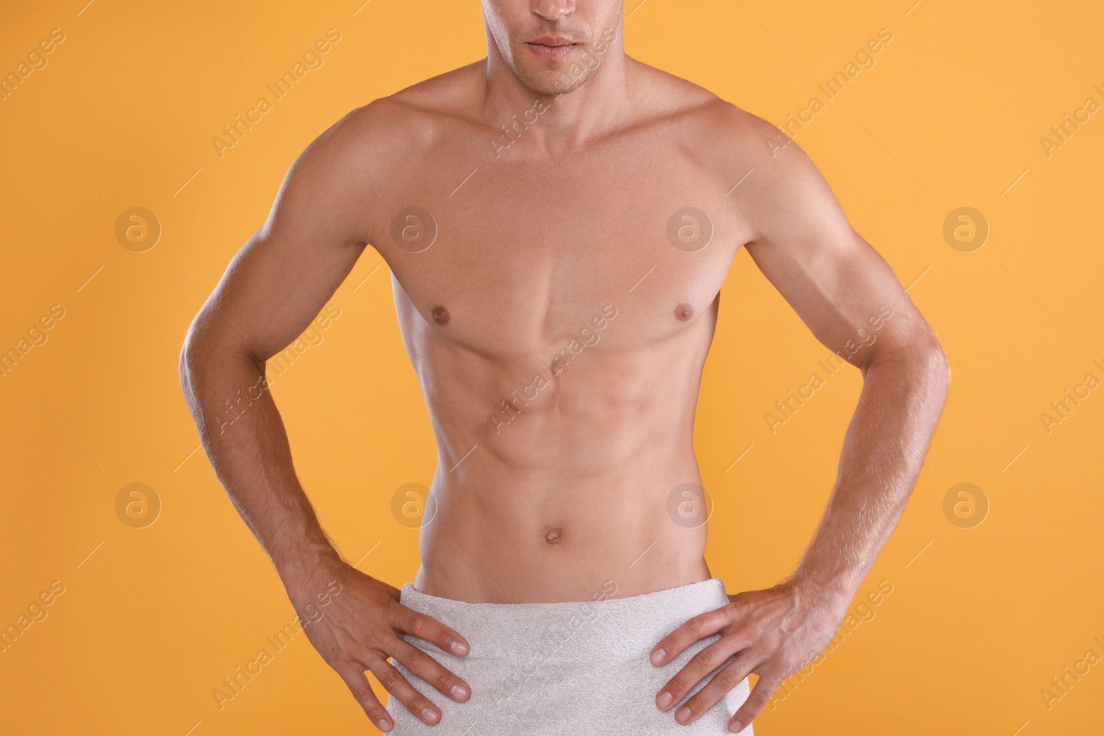 Photo of Shirtless man with slim body and towel wrapped around his hips on yellow background, closeup