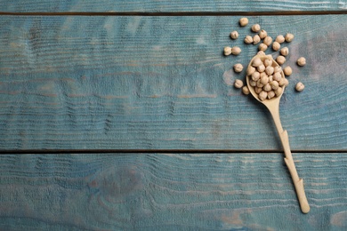 Photo of Raw chickpeas with spoon on blue wooden table, flat lay. Space for text