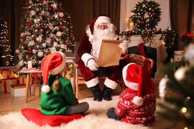 Photo of Santa Claus with wish list and children in room decorated for Christmas