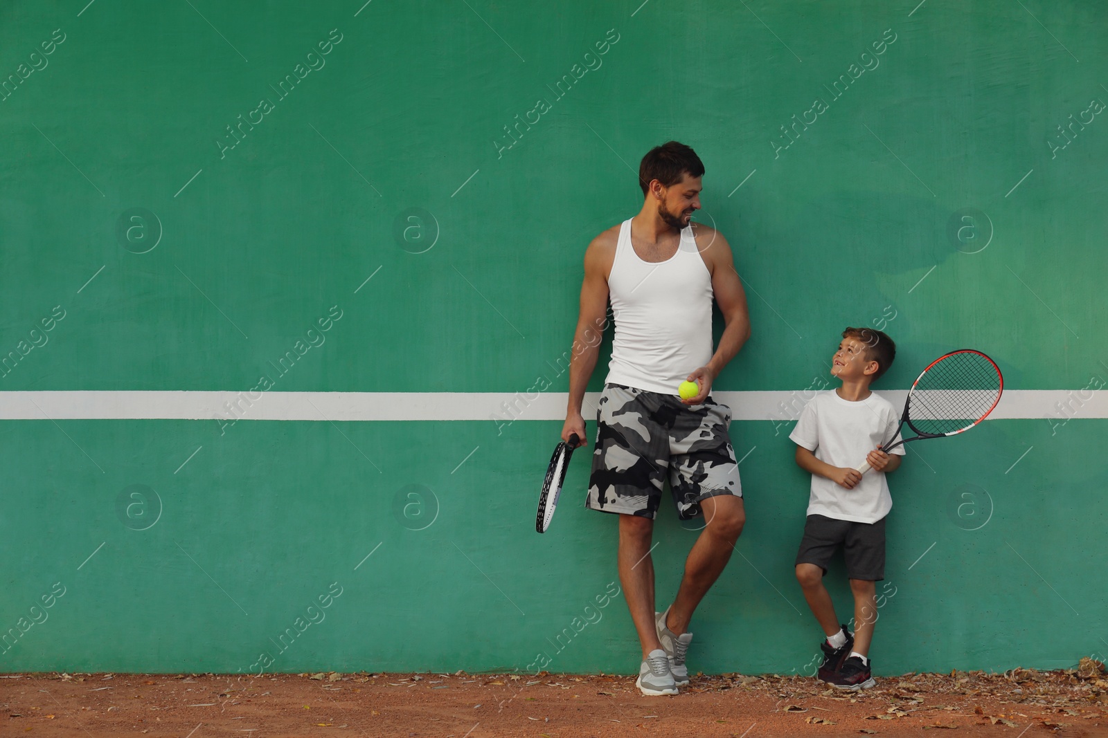 Photo of Father with his son near green wall on tennis court. Space for text