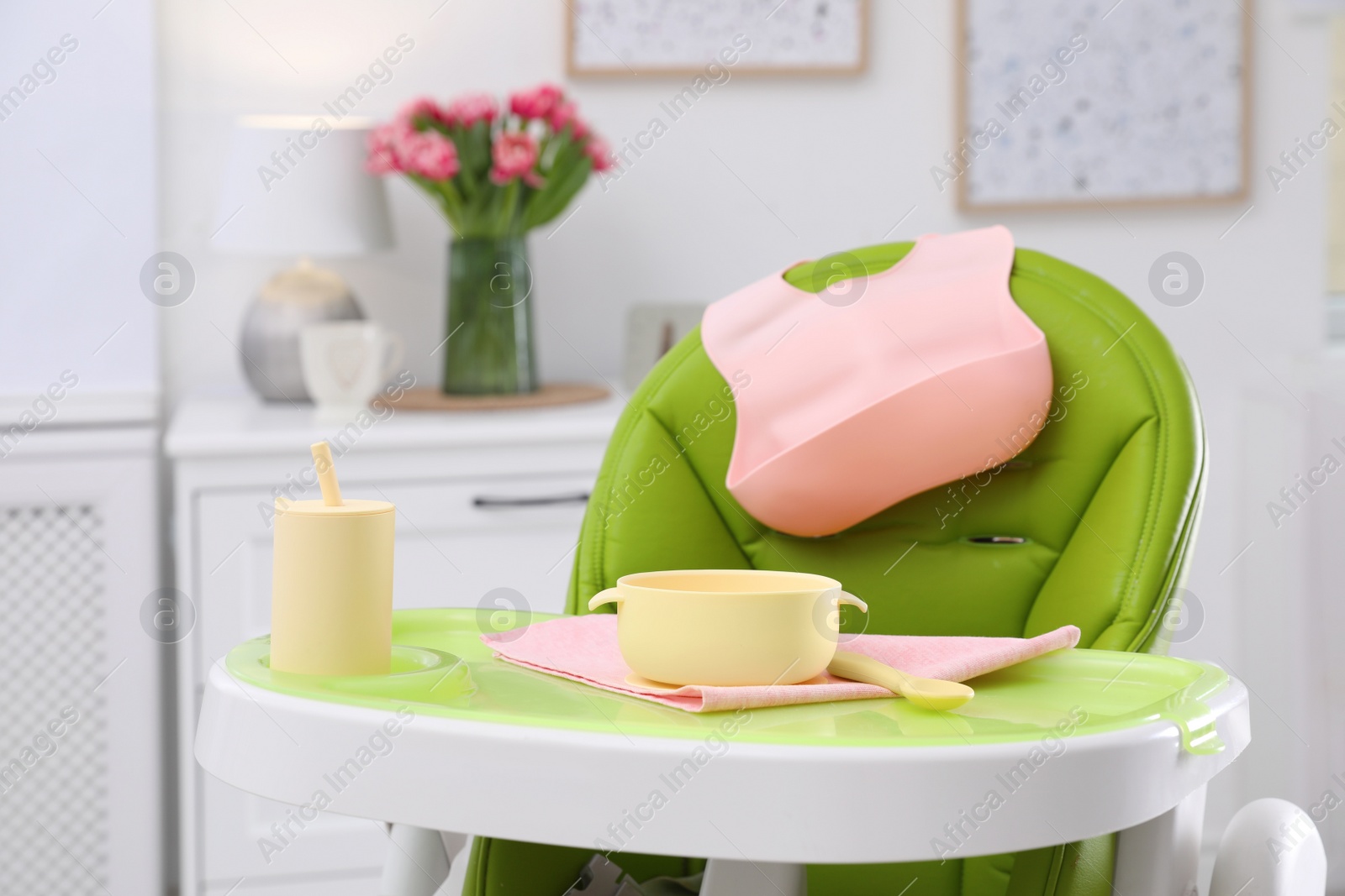 Photo of High chair with set of baby tableware on tray indoors