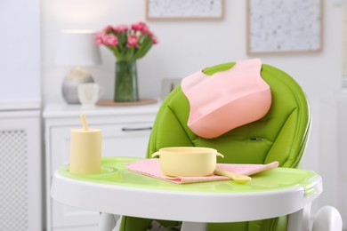 High chair with set of baby tableware on tray indoors