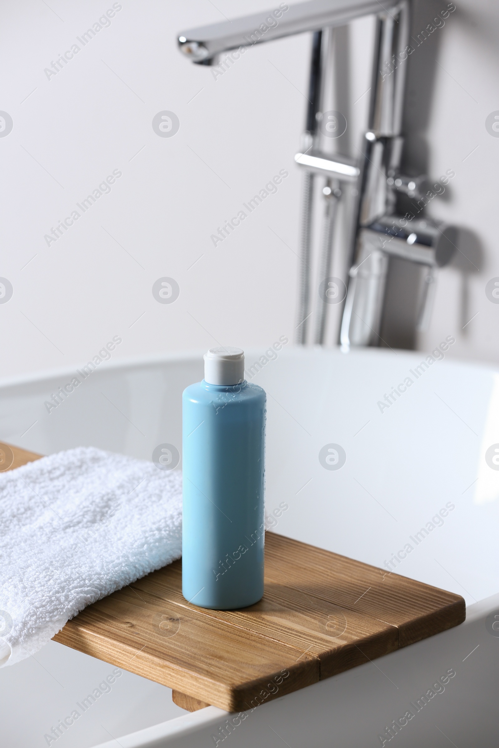 Photo of Tray with bottle of bubble bath and towel on tub in bathroom