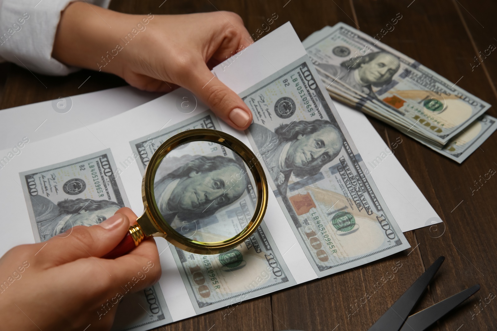 Photo of Counterfeiter examining sheet of paper with dollar banknotes at wooden table, closeup. Fake money concept