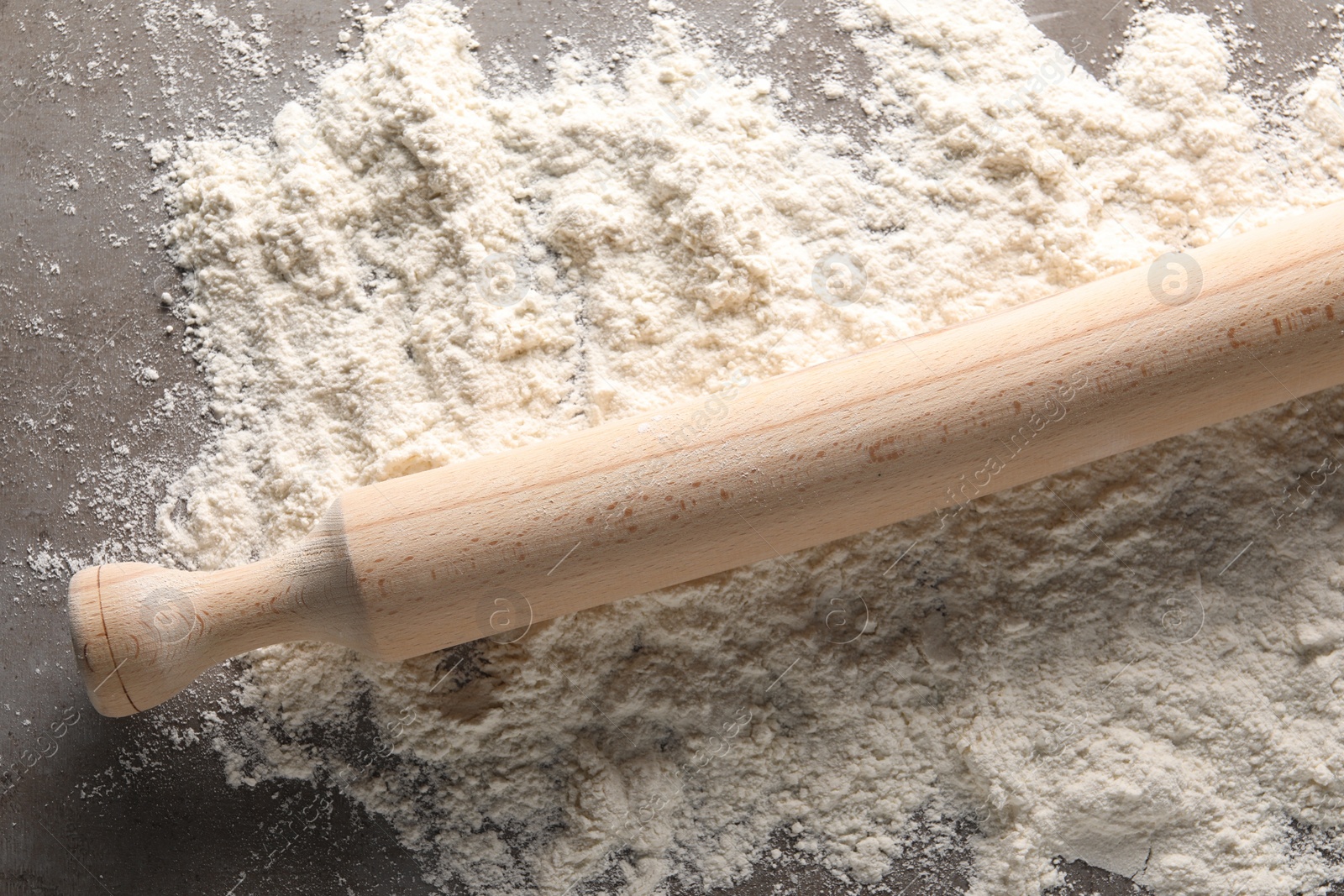 Photo of Scattered flour and rolling pin on grey textured table, top view