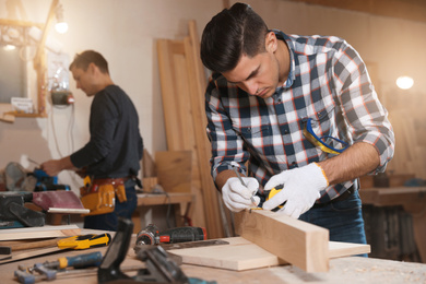 Professional carpenter and colleague working with wooden plank in workshop