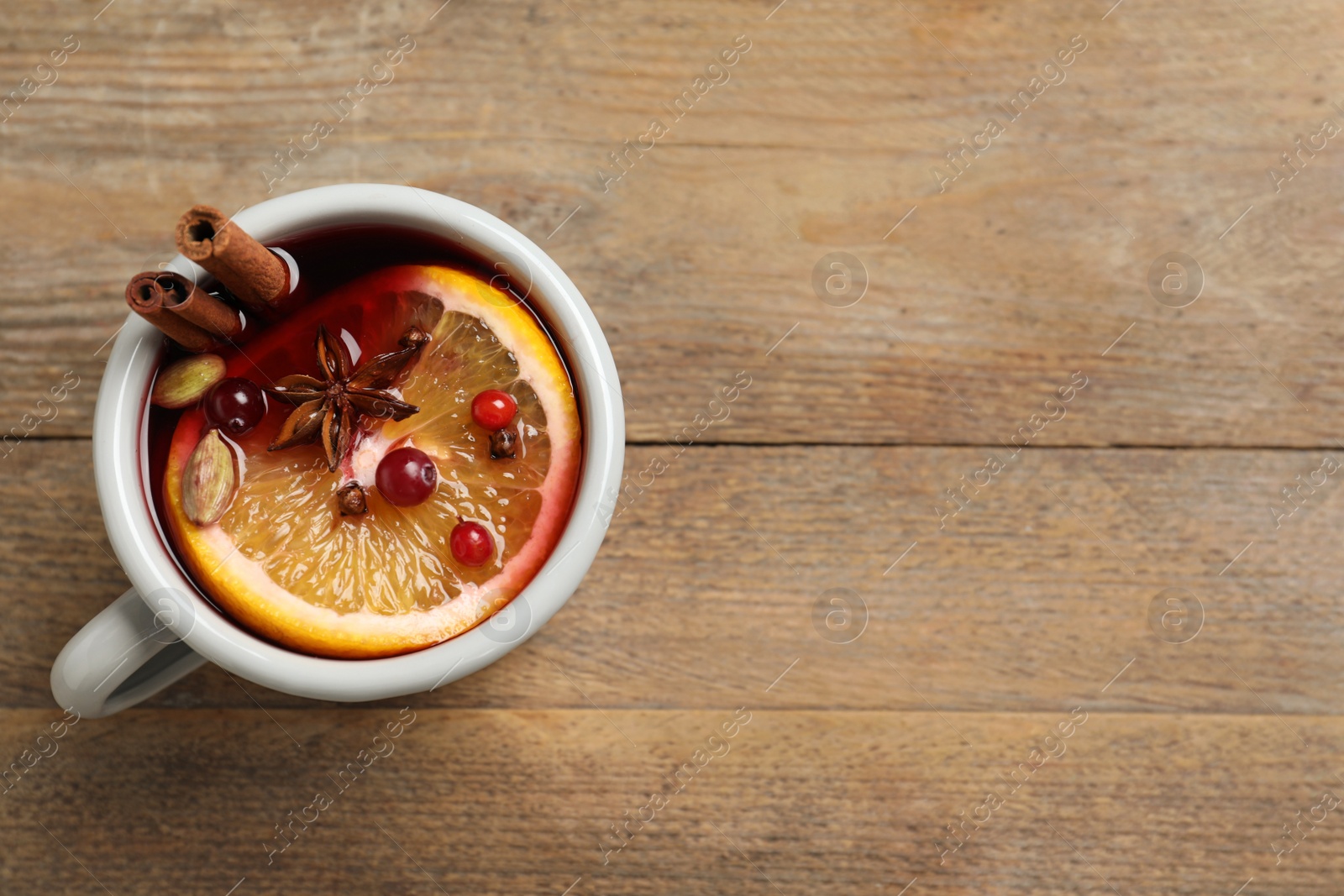 Photo of Cup of tasty mulled wine on wooden table, top view. Space for text