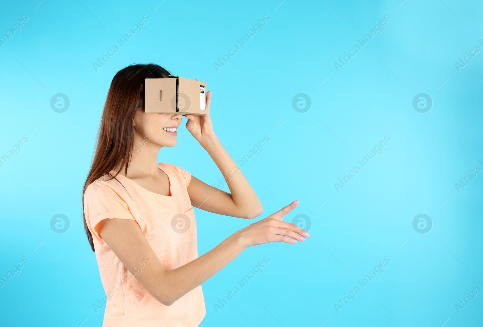 Photo of Young woman using cardboard virtual reality headset on color background. Space for text