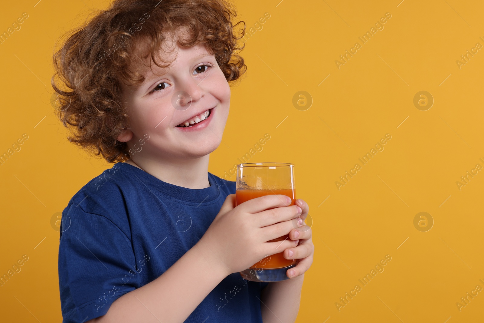 Photo of Cute little boy with glass of fresh juice on orange background, space for text