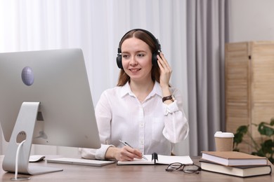 Photo of E-learning. Young woman taking notes during online lesson at wooden table indoors