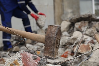 Photo of Sledgehammer on pile of broken stones. Man working outdoors, selective focus