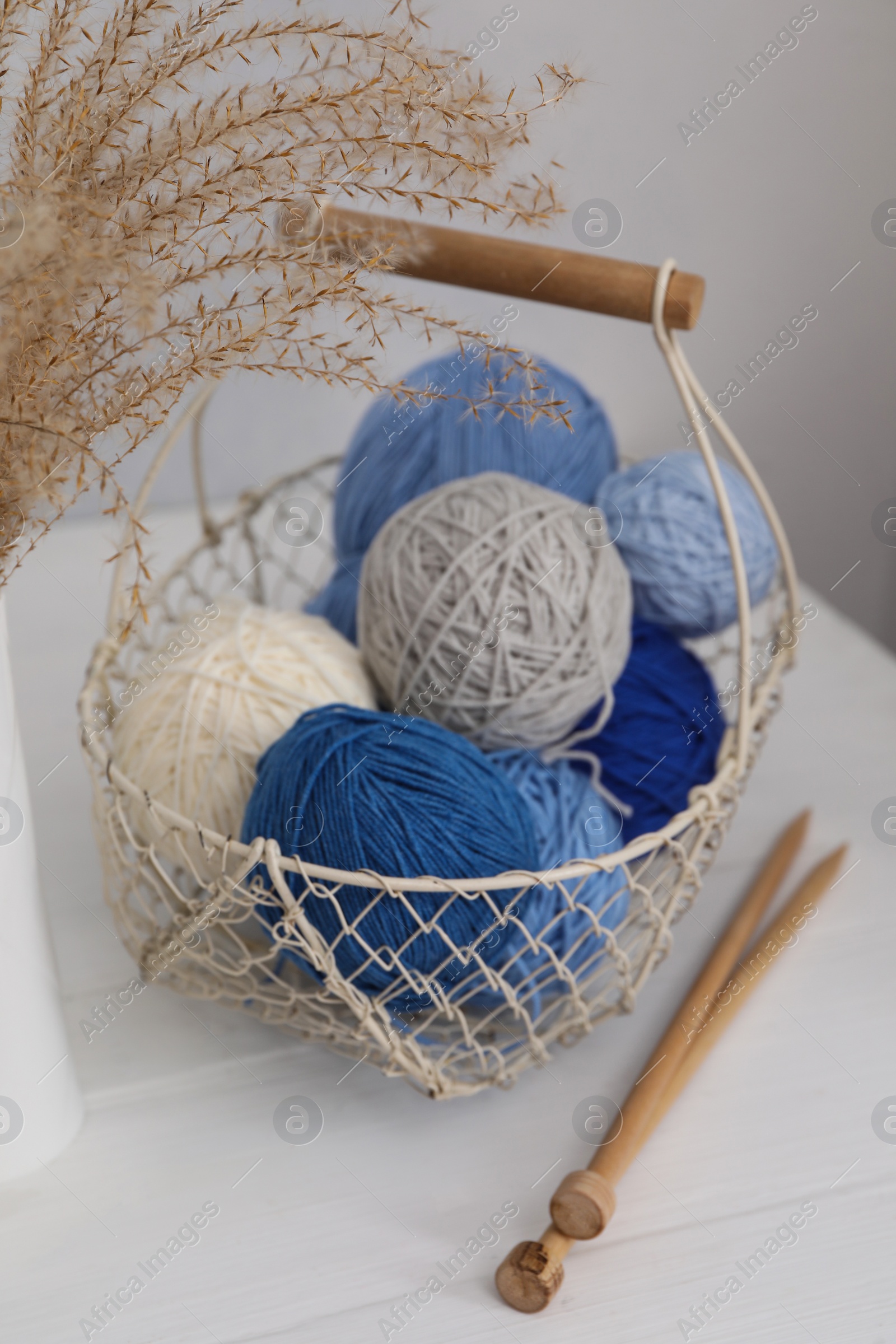 Photo of Woolen yarns in basket and knitting needles on white wooden table