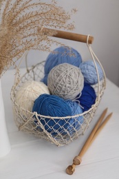 Photo of Woolen yarns in basket and knitting needles on white wooden table