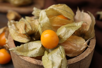 Ripe physalis fruits with calyxes in wooden bowl on table, closeup