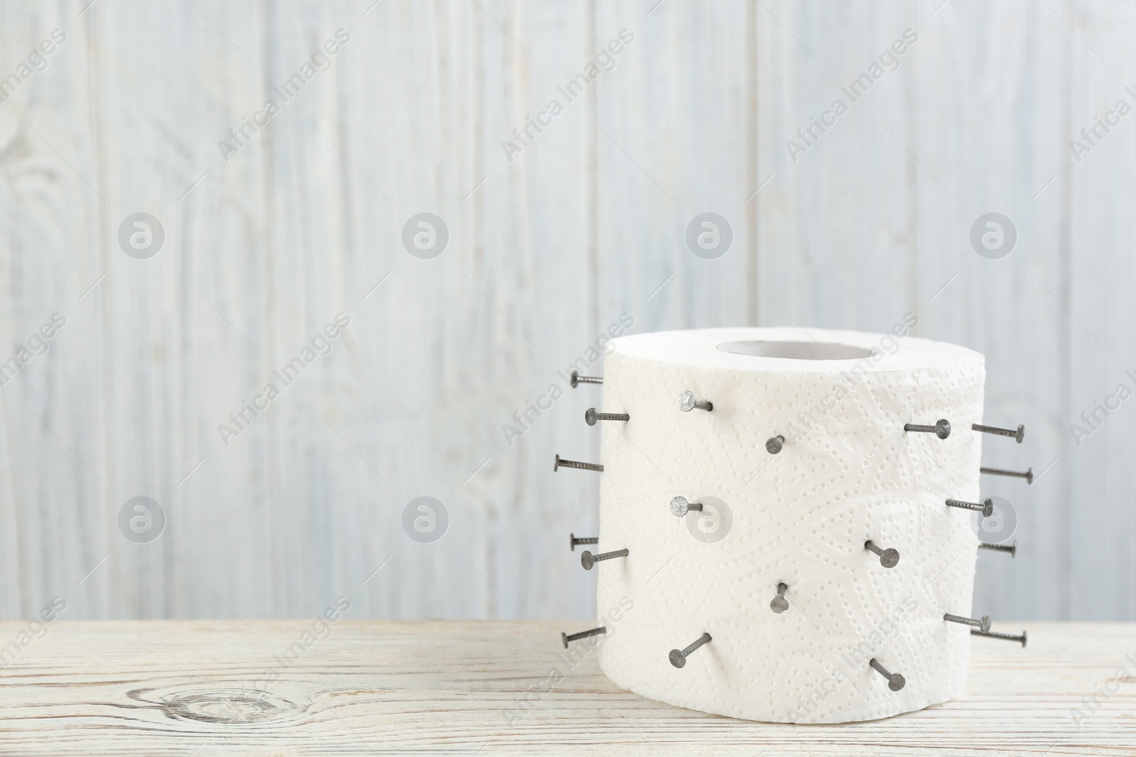 Photo of Roll of toilet paper with nails on white wooden table, space for text. Hemorrhoid problems