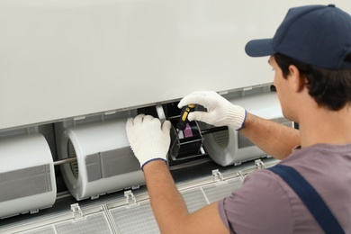 Photo of Male technician repairing air conditioner indoors