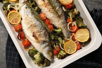 Delicious fish with vegetables and lemon in baking dish on grey table, top view