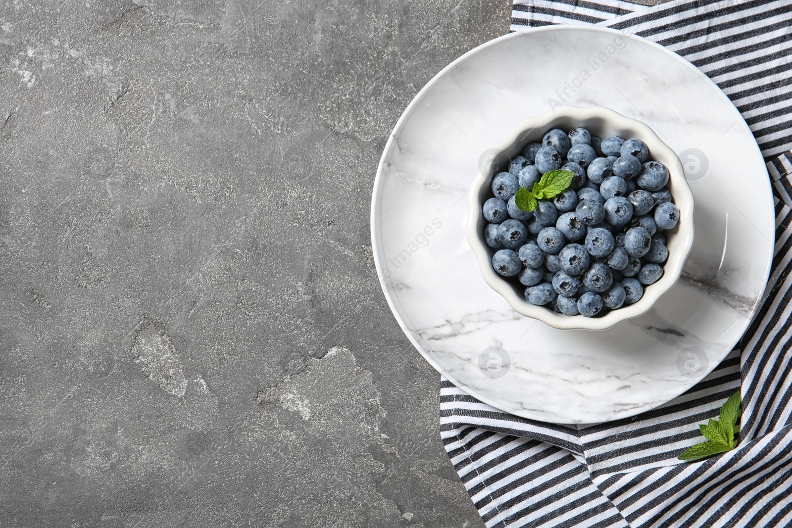 Photo of Dishware with juicy blueberries and space for text on color table, top view