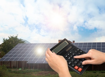 Image of Woman using calculator against house with installed solar panels. Renewable energy and money saving