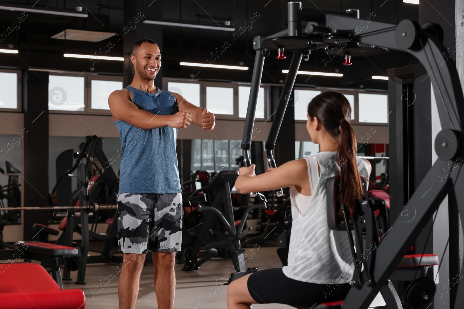 Photo of Happy trainer explaining woman how to do exercise properly in modern gym