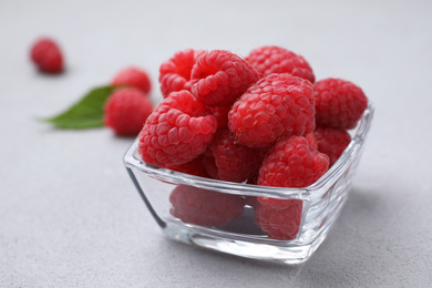 Photo of Delicious fresh ripe raspberries in glass bowl on grey table, closeup