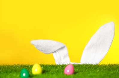 Photo of Easter eggs on green lawn and funny bunny ears against color background, space for text