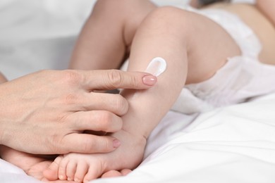 Woman applying body cream onto baby`s leg on bed, closeup