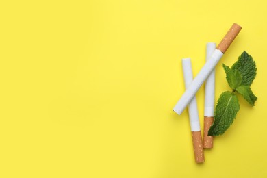 Photo of Menthol cigarettes and mint on yellow background, flat lay. Space for text
