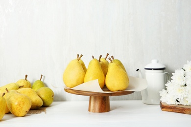 Stand with fresh ripe pears on table against light background