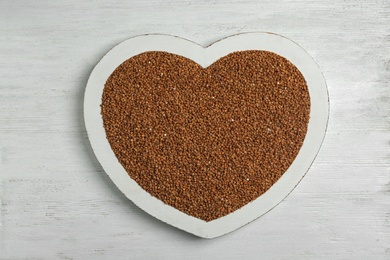 Photo of Heart shaped tray with raw buckwheat on wooden background, top view