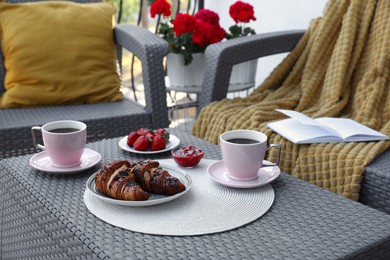 Outdoor breakfast with tea and croissants on rattan table on terrace