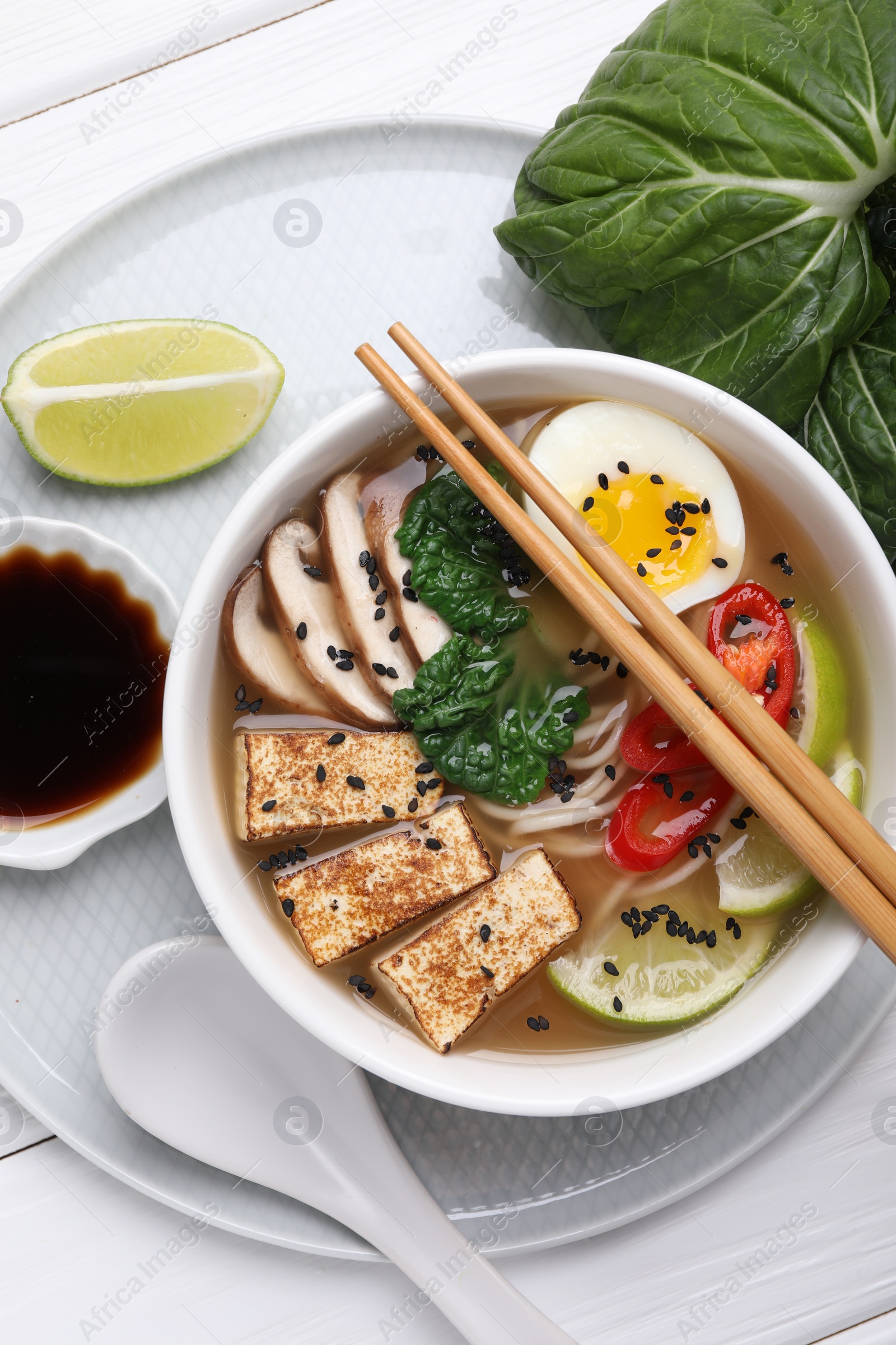 Photo of Delicious vegetarian ramen, soy sauce and pak choy leaves on white wooden table, top view