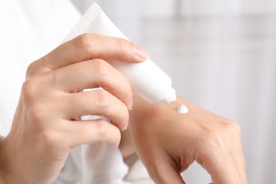 Photo of Woman in bathrobe applying moisturizing hand cream, closeup. Winter skin care cosmetic