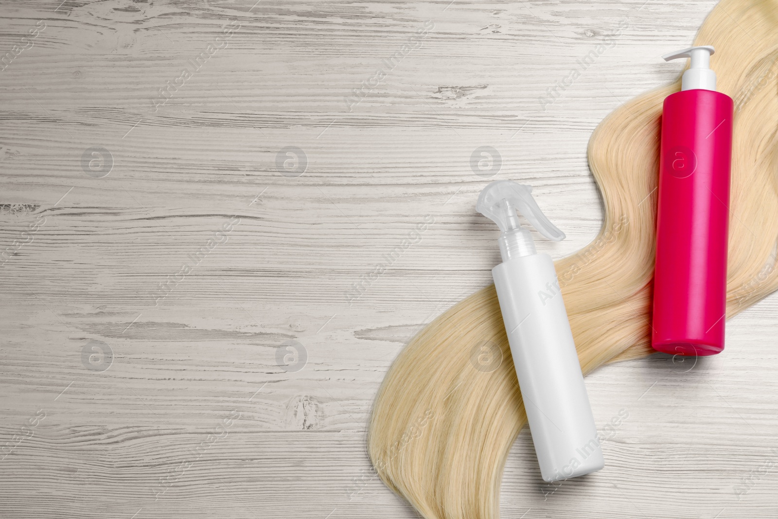 Photo of Spray bottles with thermal protection and lock of blonde hair on white wooden table, flat lay. Space for text