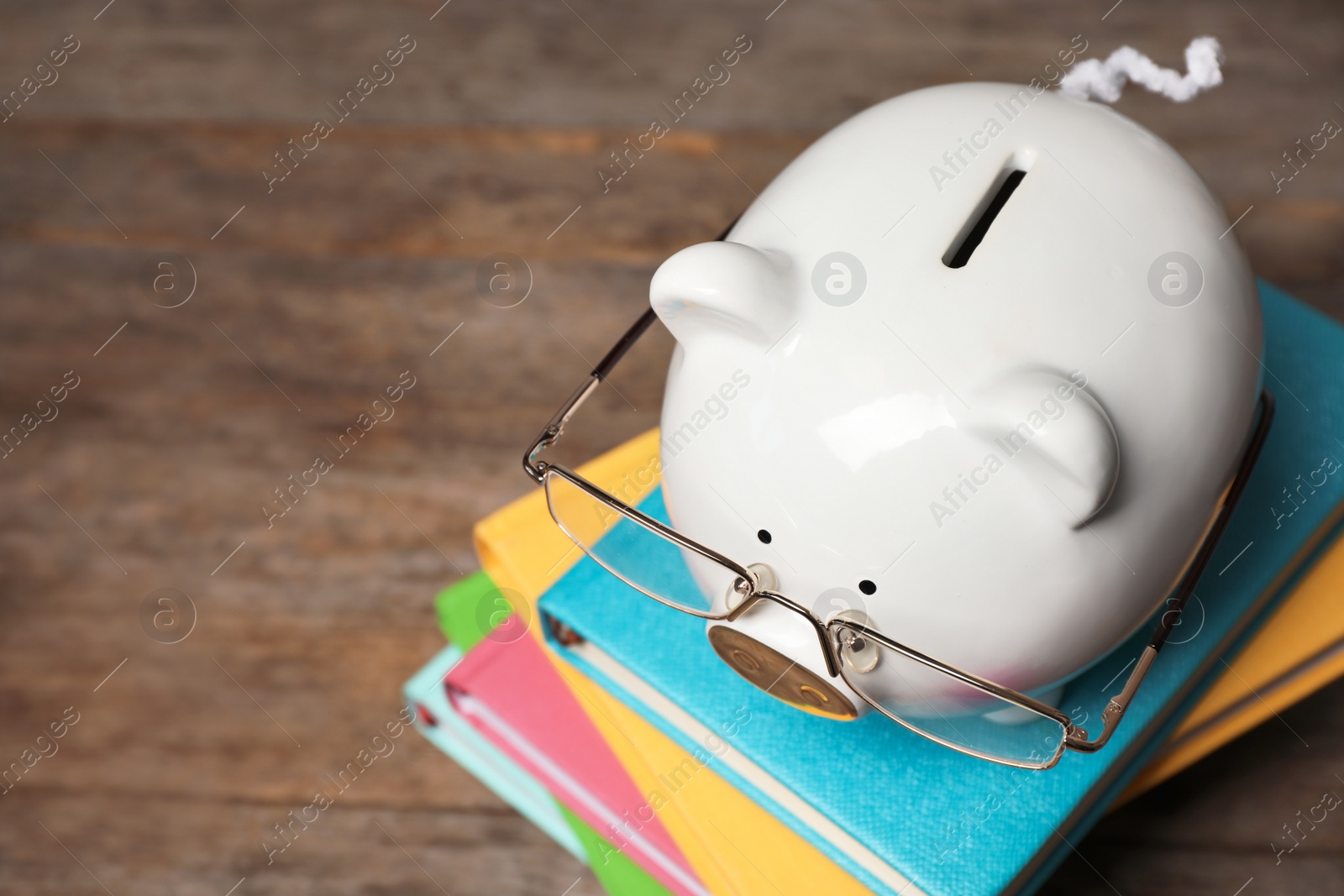 Photo of Piggy bank with glasses and books on wooden table. Space for text